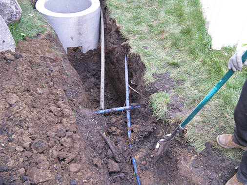 Carefully digging around underground water lines to install drainage correction components